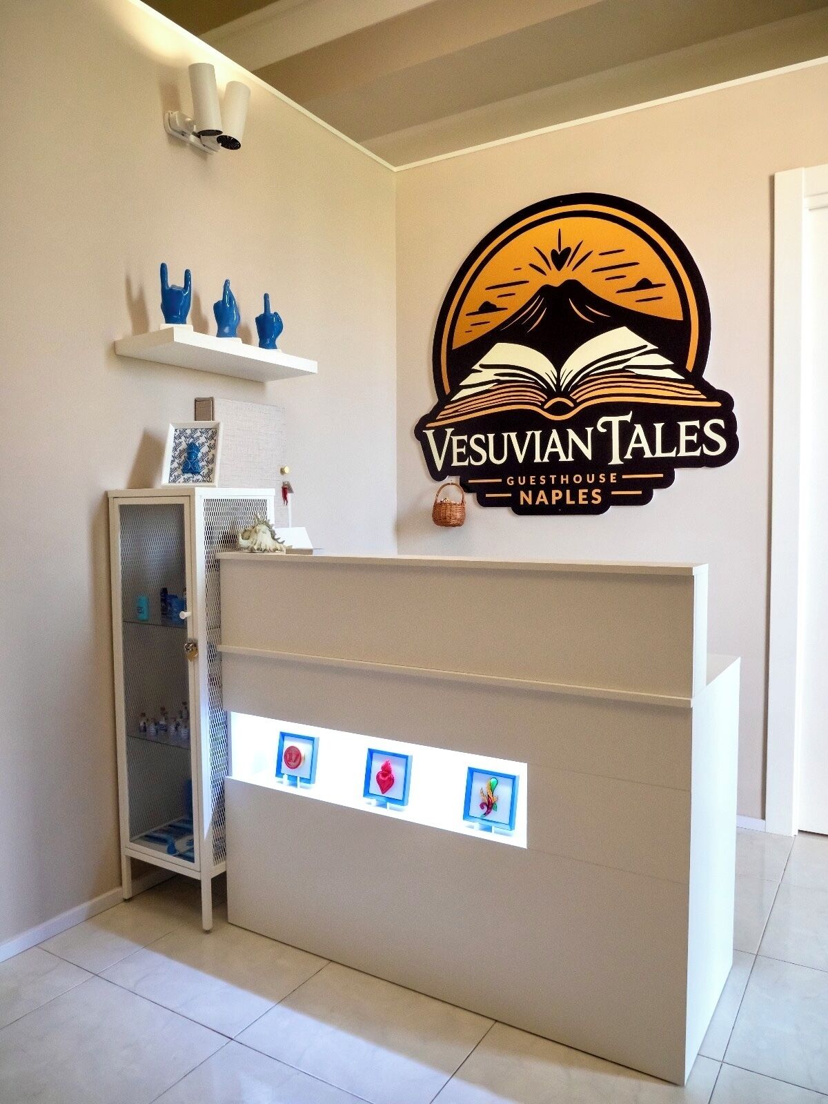Un comptoir d’accueil orné du logo de la « Maison d’hôtes Vesuviian Tales à Naples » et une étagère avec des objets décoratifs.