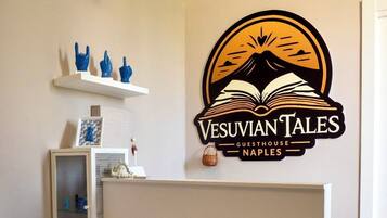 Un comptoir d’accueil orné du logo de la « Maison d’hôtes Vesuviian Tales à Naples » et une étagère avec des objets décoratifs.