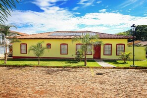 A yellow building with a red door and windows, surrounded by a cobblestone street and small trees.