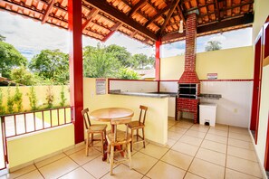 An outdoor patio with a brick oven, a table with chairs, and a view of greenery. - Casa Del Rey (Pirenópolis)