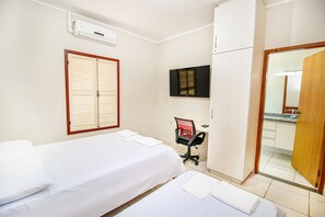 A hotel room with a bed, a desk with a chair, a television, and an air conditioning unit. - Casa Del Rey (Pirenópolis)