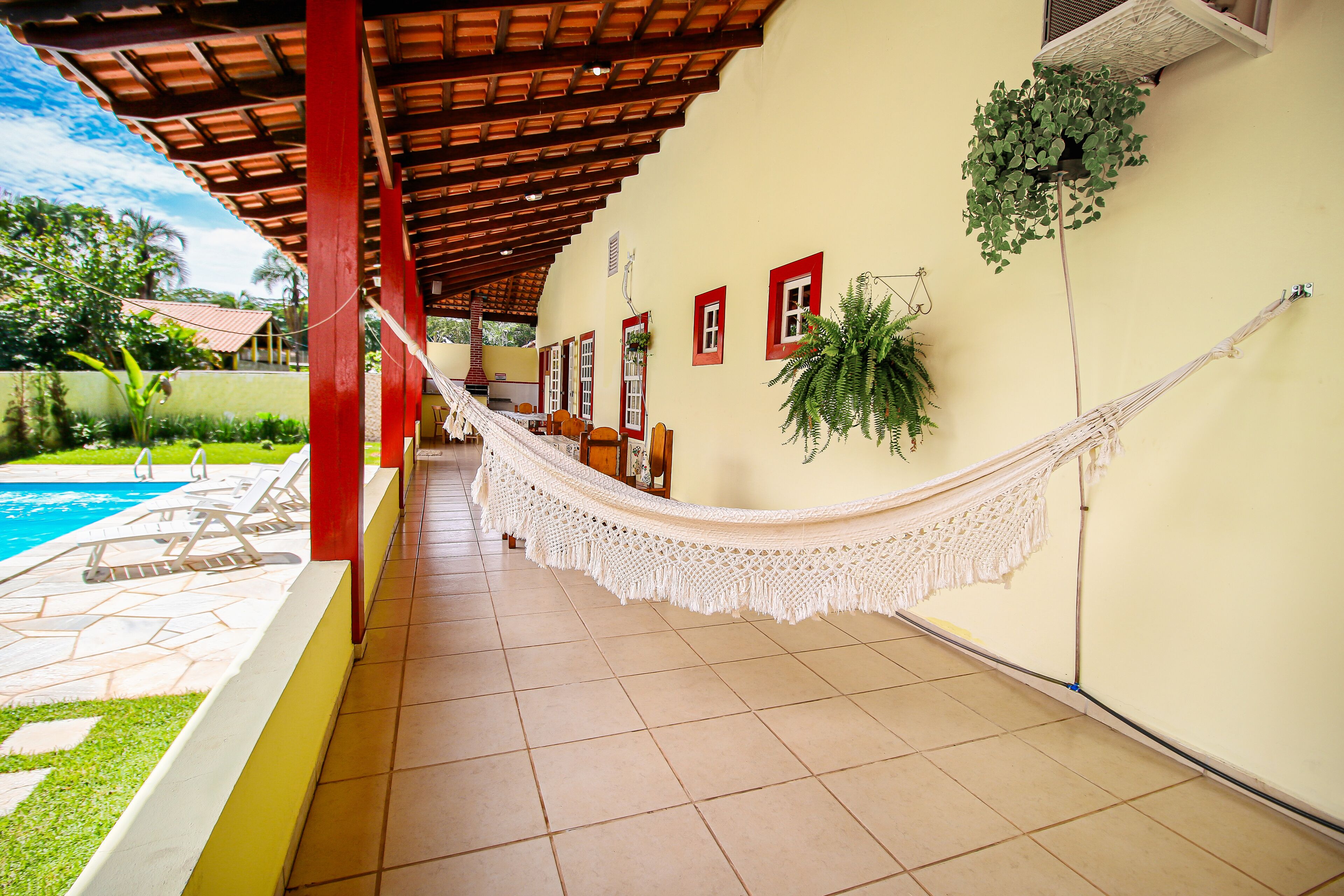 A covered outdoor area with a hammock, poolside chairs, and a tiled floor.