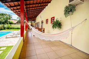 A covered outdoor area with a hammock, poolside chairs, and a tiled floor.