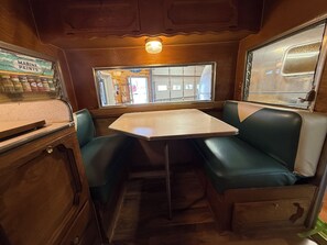 A compact interior with a table and two green cushioned seats, a window with a view, and a cabinet with marine paints.