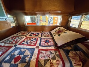 A cozy room with a large bed featuring a patchwork quilt, a window with a view of the outside, and a wooden ceiling.
