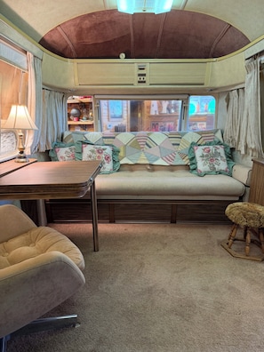 A cozy interior with a sofa, a table, and a chair, featuring a window with curtains.