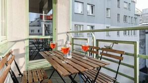 Varanda com mesas e cadeiras de madeira, dois copos de vinho tinto e vista para um edifício com várias janelas.