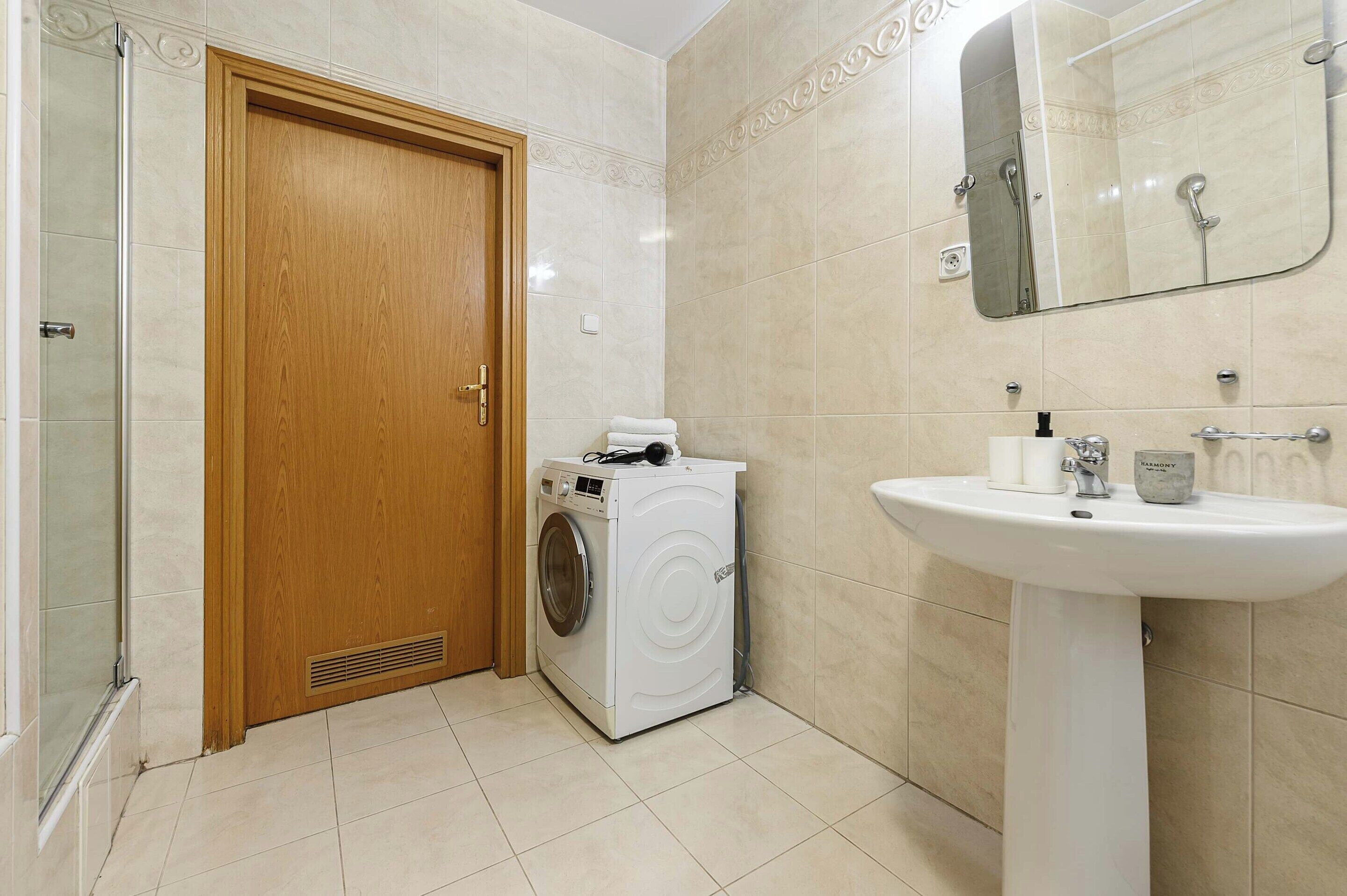A bathroom with a wooden door, a washing machine, a sink, and a mirror.