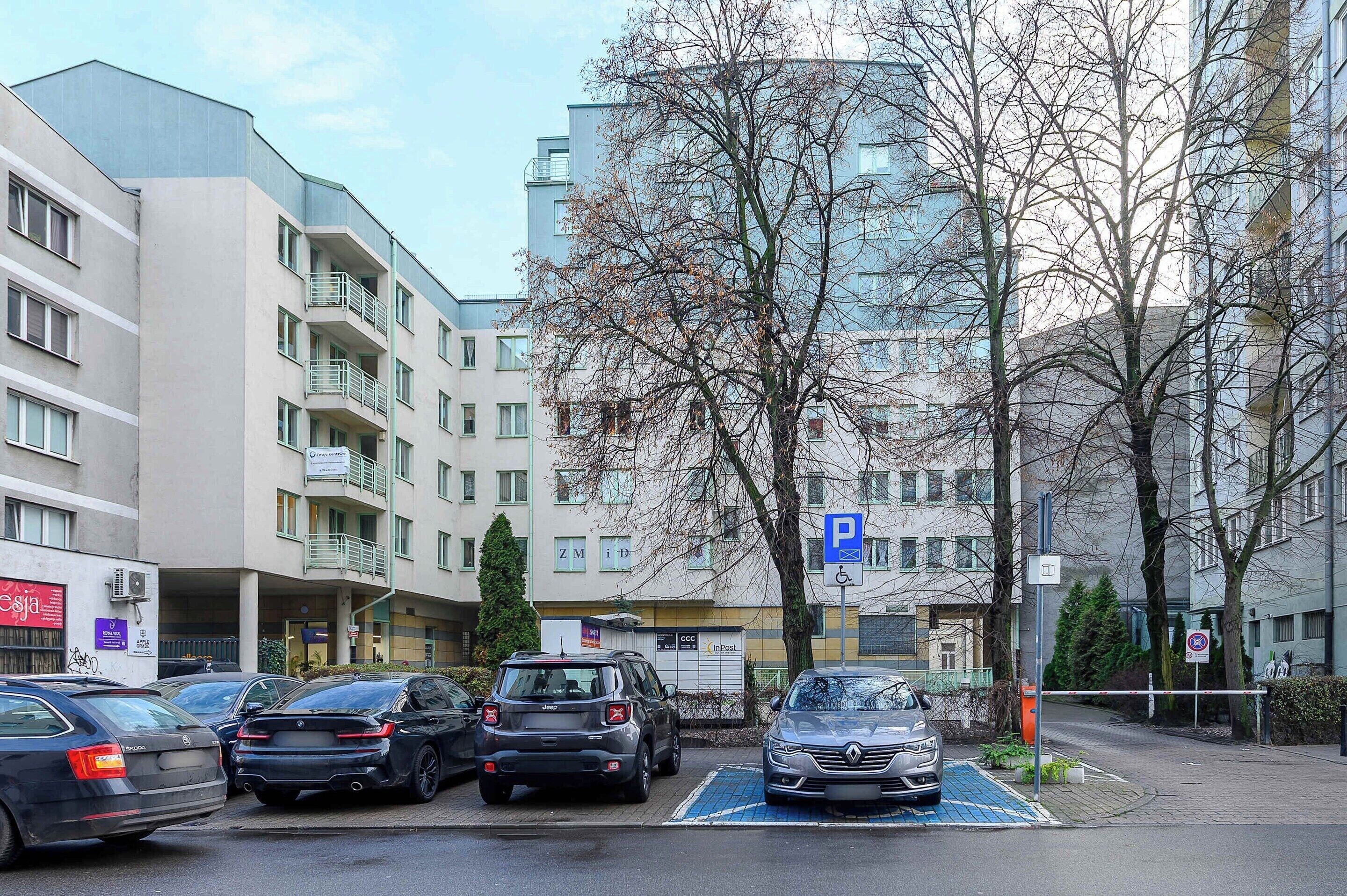 A parking area with cars, a blue parking sign, and a building with multiple floors and balconies.