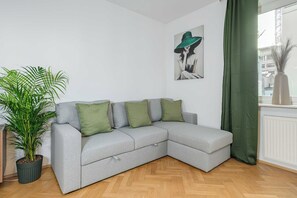 A grey sectional sofa with green cushions, a potted plant, and a painting on the wall. - Stylish Warsaw Apartment With Balocny (Warsaw)