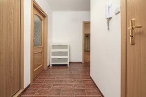 A hallway with wooden doors, a white shelf unit, and a thermostat on the wall. - Stylish Warsaw Apartment With Balocny (Warsaw)