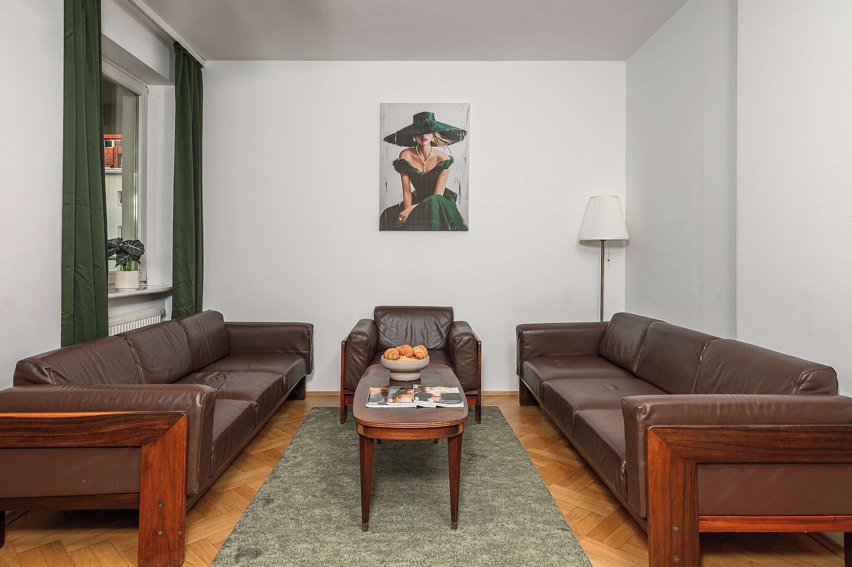 A living room with two brown leather sofas, a wooden coffee table with magazines and croissants, a floor lamp, and a painting on the wall.