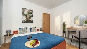 Quarto com cama, mesa de cabeceira, escrivaninha, cadeira, espelho e um quadro na parede.