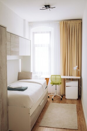 Een slaapkamer met een bed, bureau, stoel en een raam met gordijnen.