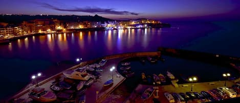 Un puerto deportivo al atardecer con barcos amarrados y un horizonte urbano de fondo.