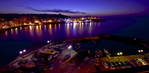 A marina at dusk with boats docked and a cityscape in the background. - Lovely 3-bedroom Hillock maisonette in Marsalforn with AC, pool and BBQ yard (Żebbuġ)
