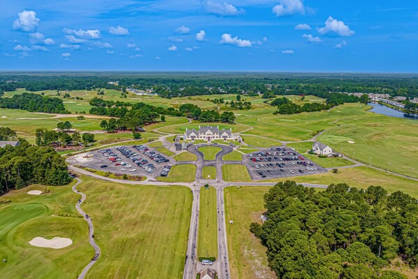 Vista aérea de un campo de golf con un club house, zonas de estacionamiento y follaje circundante.