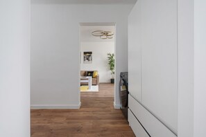 Ein Korridor mit Holzboden, der in einen Wohnbereich mit Sofa, Couchtisch und Pflanze führt.