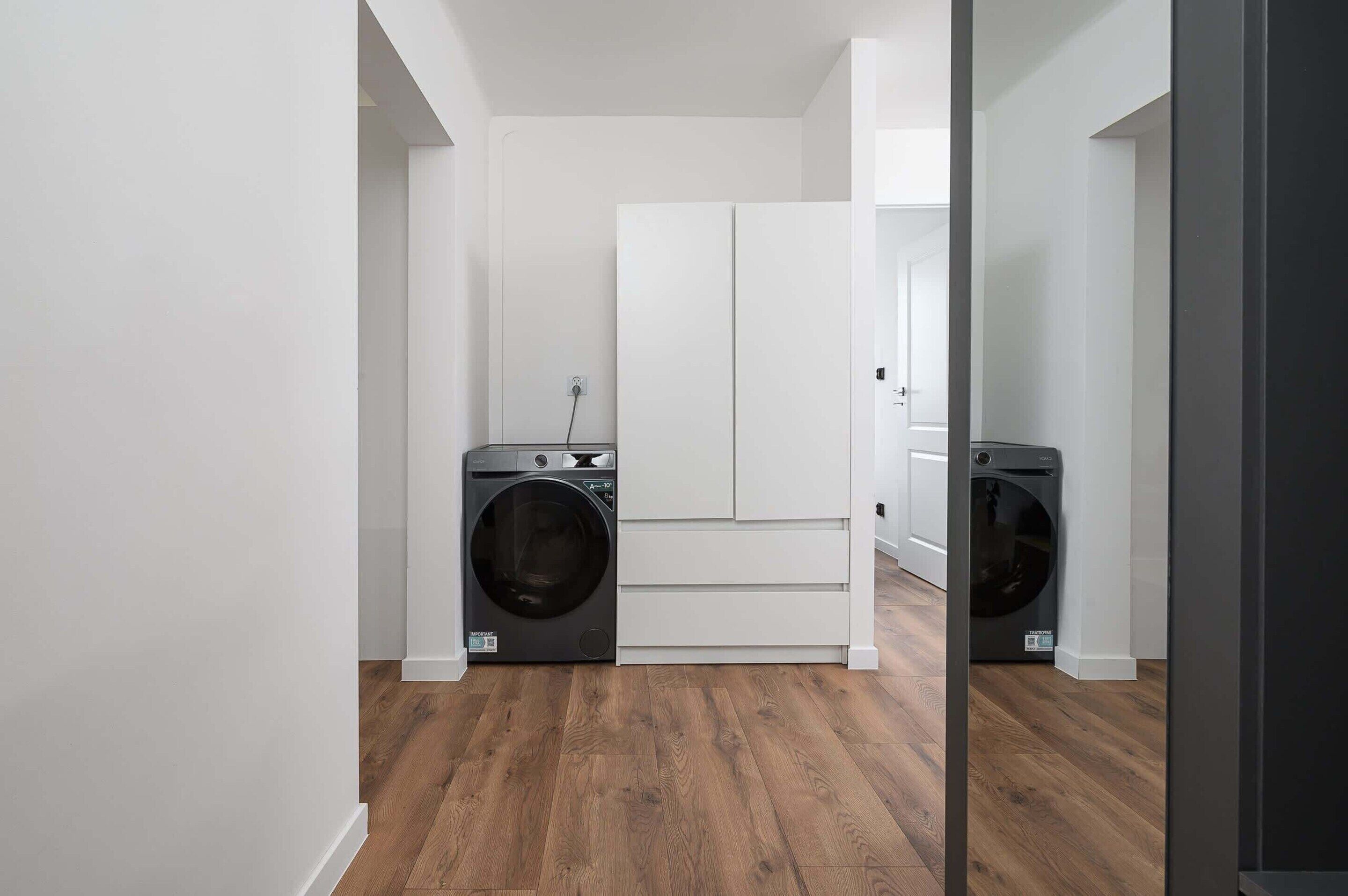 A laundry room with two front-loading washing machines, a white door, and wooden flooring.
