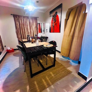 Un comedor con una mesa dispuesta para cuatro, una silla negra, un bolso rojo y un cuadro colgado en la pared.