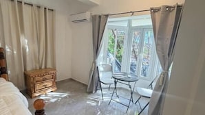Un dormitorio con una cama, una mesita de noche de madera, una pequeña mesa y una ventana con cortinas.