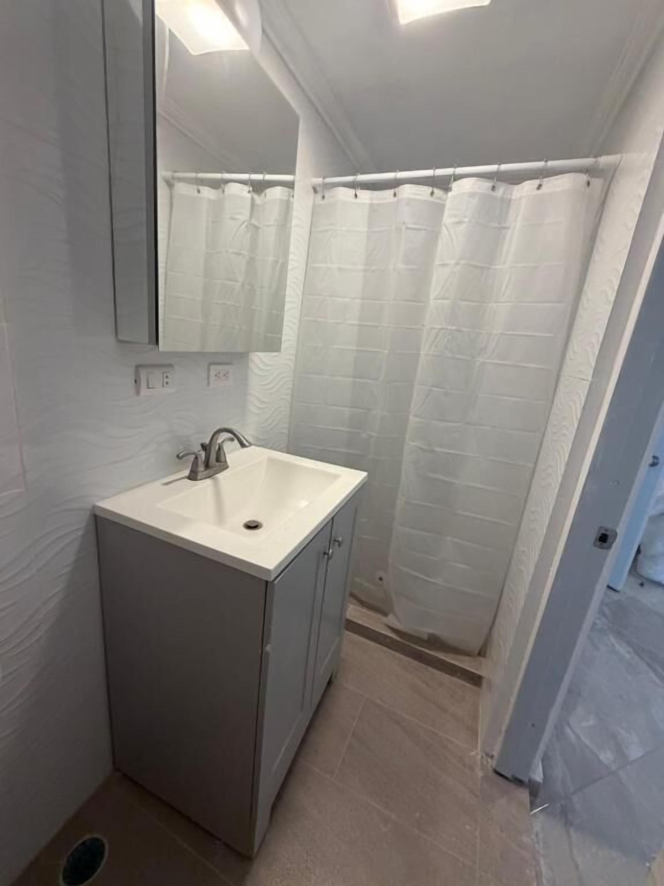 Un baño con un lavamanos blanco, un espejo y una cortina de ducha.