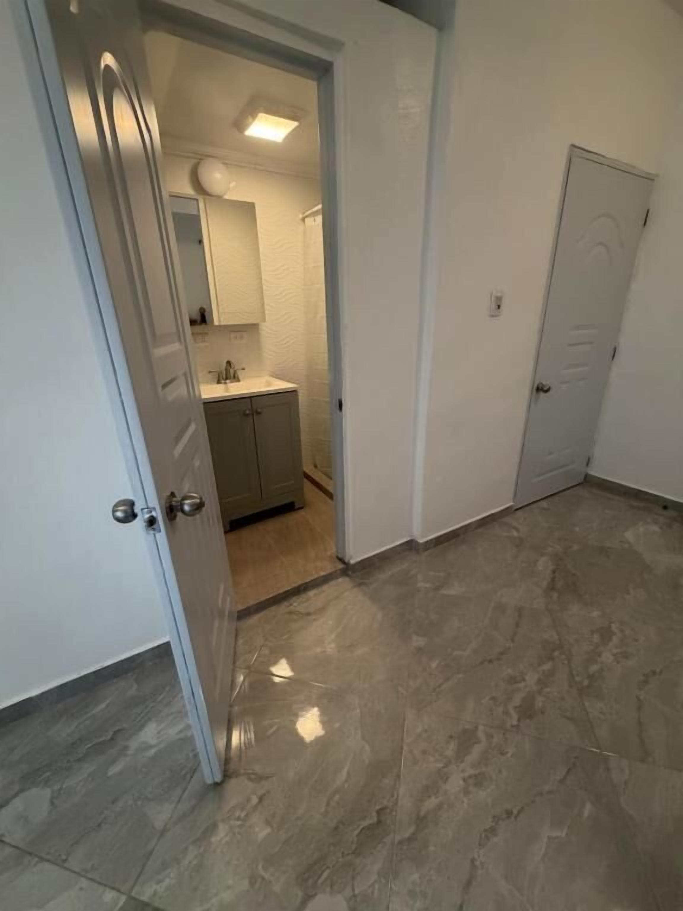 A hallway leading to a bathroom with a mirror, sink, and cabinets.