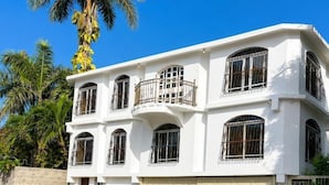 Un edificio de dos pisos con fachada blanca, numerosas ventanas con rejas y un garaje.