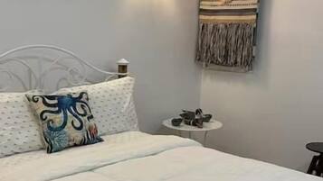 Quarto com uma cama, uma luminária na parede, uma pequena mesa redonda com abajur e um ornamento decorativo na parede.