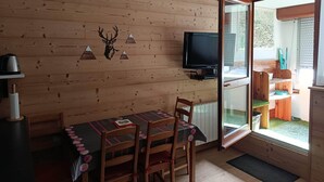 Een houten interieur met een tafel, stoelen, een opgehangen hertenkop en een televisie.