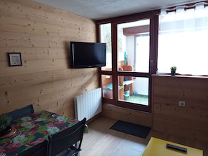 A room with a wooden interior, a television mounted on the wall, a dining table with chairs, and a window with a view of the outside. - Apartment in Saint-Lary Village (Saint-Lary-Soulan)