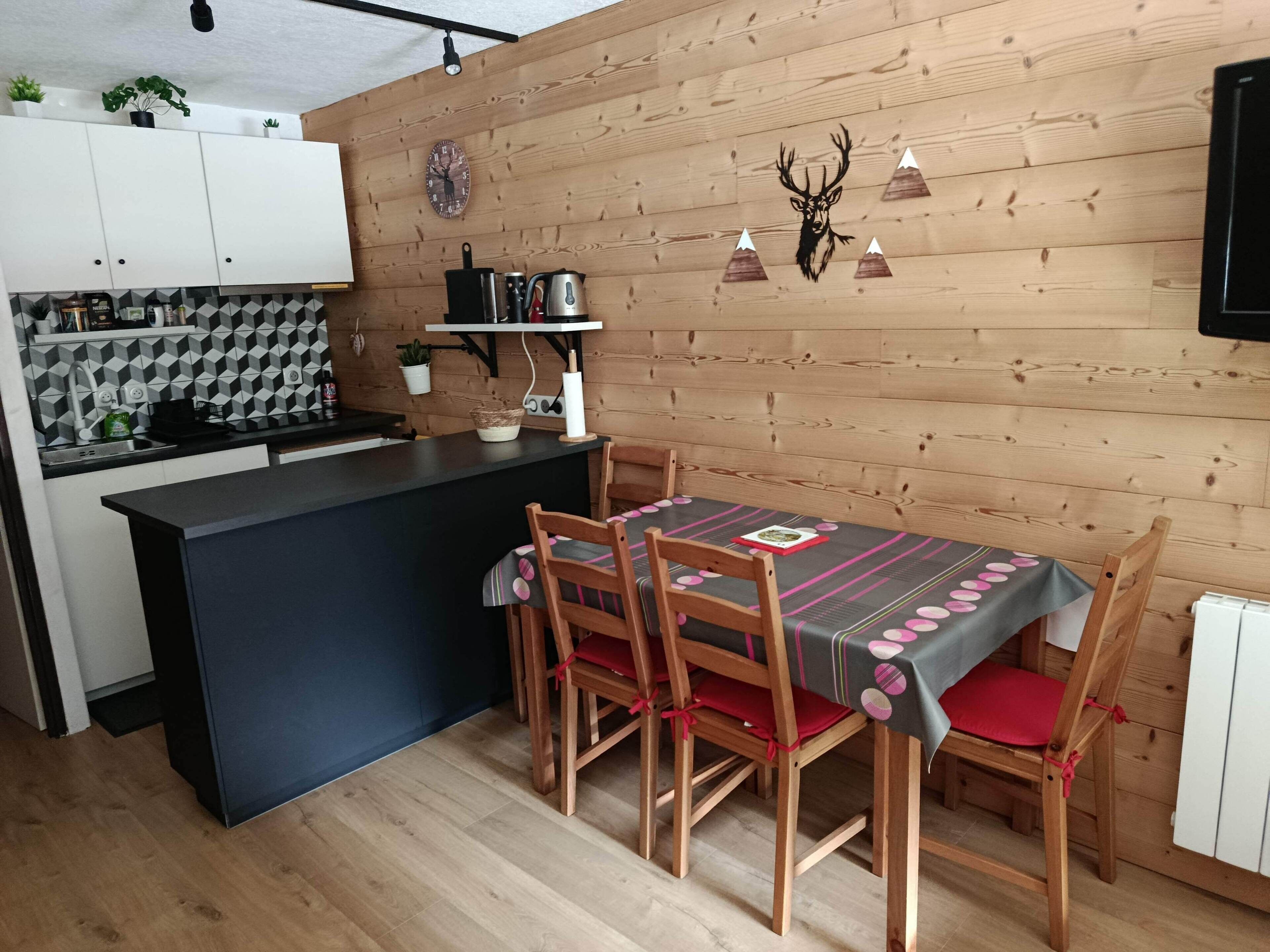 A modern kitchen with wooden paneling, a black countertop, and a dining area with a table and chairs.