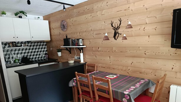 Een moderne keuken met houten lambrisering, een zwart aanrecht en een eethoek met een tafel en stoelen.