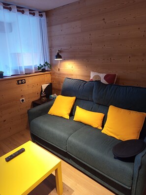 A cozy living room with a green sofa, yellow cushions, a wooden wall, a small table, and a lamp. - Apartment in Saint-Lary Village (Saint-Lary-Soulan)