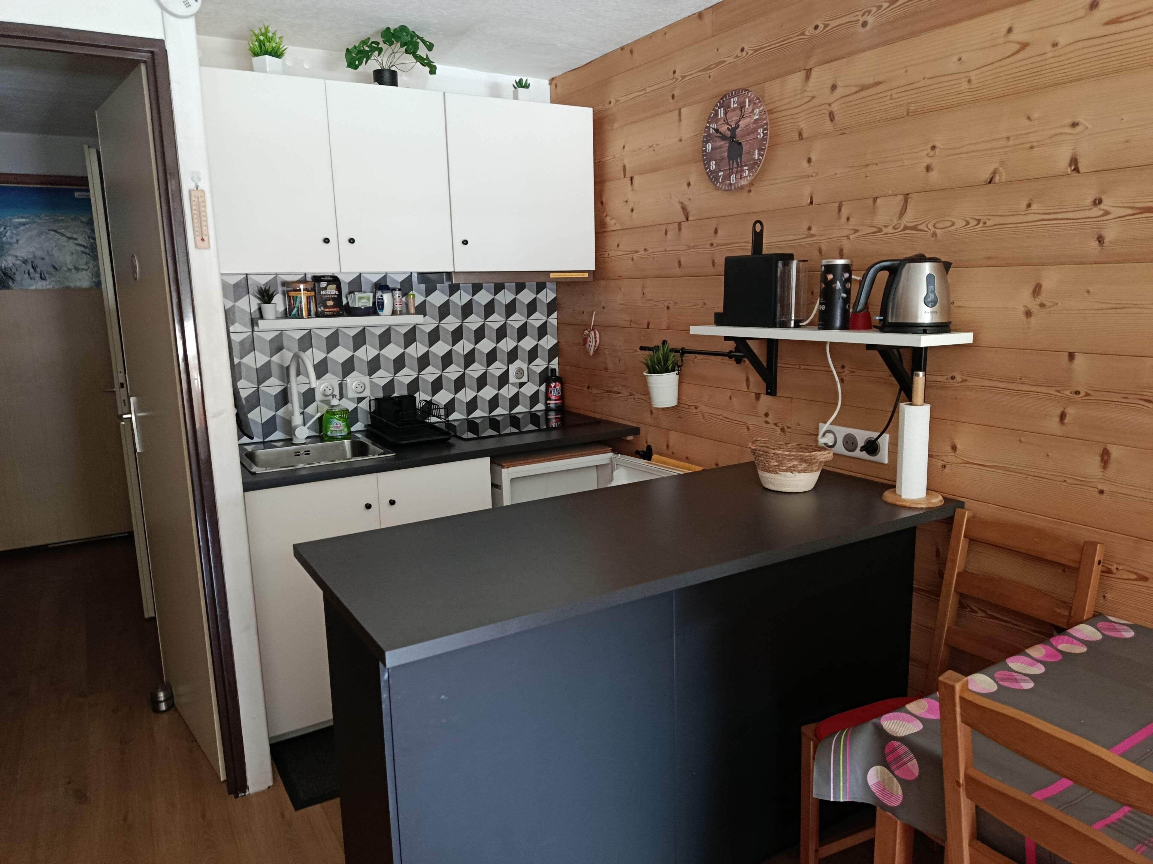 Una cocina compacta con alacenas blancas, encimera negra y pared de madera, además de un reloj.
