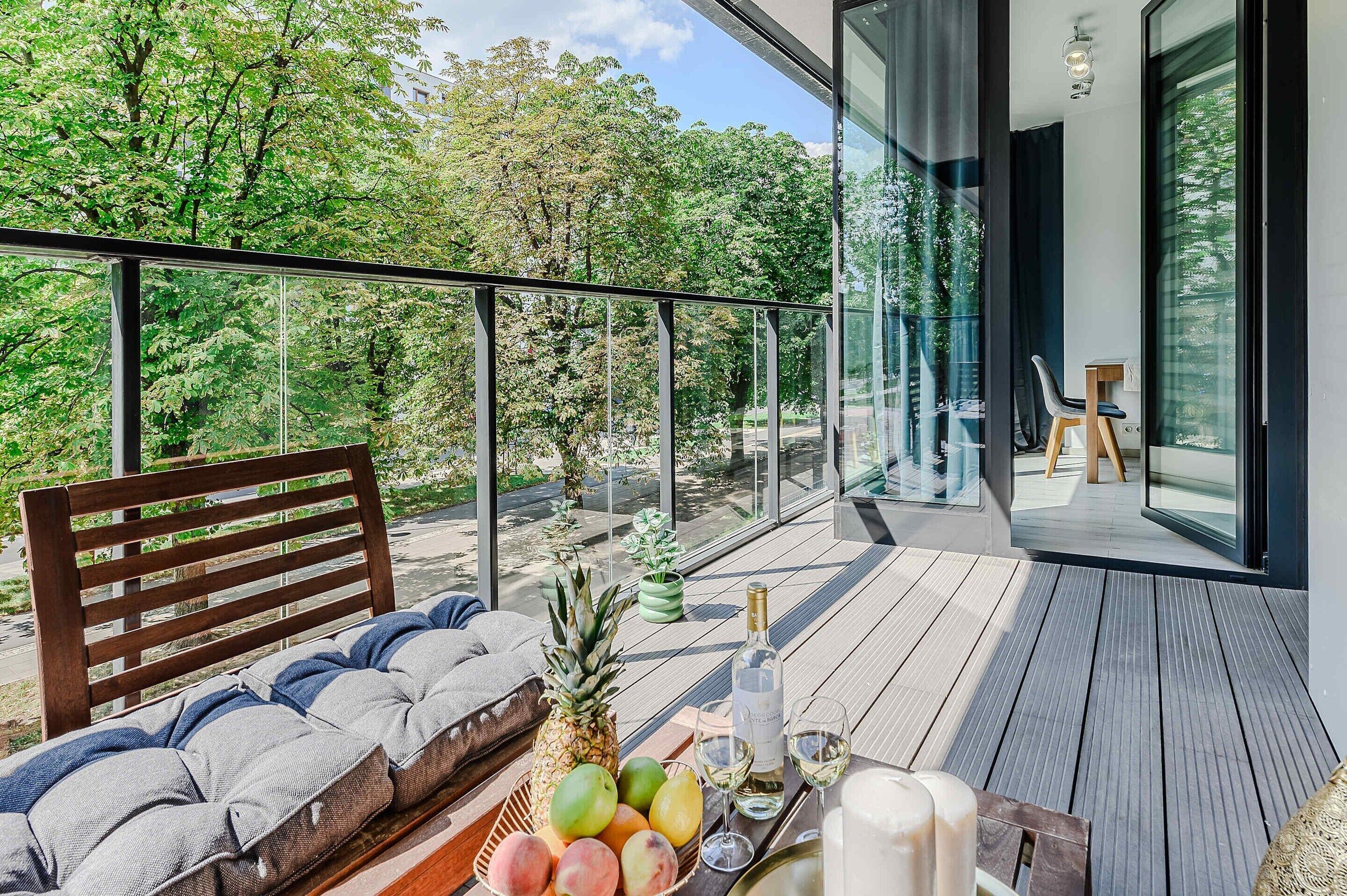 A modern outdoor seating area with a wooden bench, a table with fruits, a bottle, and glasses.