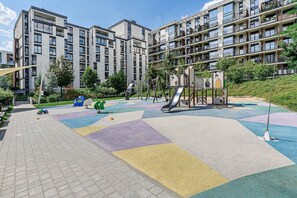 Ein Spielplatz mit Rutsche und Klettergerüsten, umgeben von einem mehrstöckigen Wohngebäude mit Balkonen.