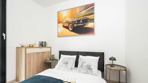 Ein Schlafzimmer mit einem Bett, einem Nachttisch, einer Lampe, einem Wandbild und einer Tür.