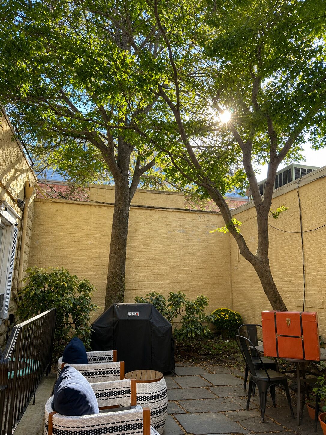 A backyard with a barbecue grill, outdoor furniture, and a tree providing shade.