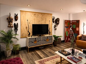 A modern living room with a flat-screen TV on a wooden cabinet, surrounded by various decorative items and plants. - Spacious 3BR Home in Heart of Montclair – Walkable, Near NYC & Newark Airport (Montclair)