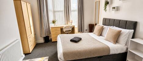 A modern bedroom with a bed, a desk, and a wardrobe.