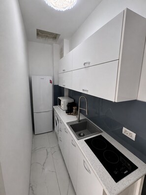 Eine kompakte Küche mit weißen Schränken, einer eingebauten Mikrowelle, einem Spülbecken und einer schwarzen Induktionskochplatte.