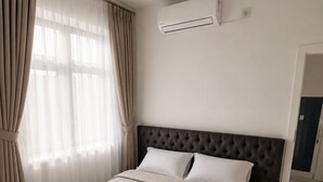 Et hotelværelse med en stor seng, en mørk sengegavl og en aircondition-enhed på væggen.
