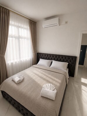 Ein Hotelzimmer mit einem großen Bett, einem dunklen Kopfteil und einer Klimaanlage an der Wand.