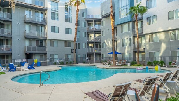 A modern apartment building with a swimming pool, lounge chairs, and palm trees. - Modern Tempe 1BR • AC + Pool + Gym • 5 Min to ASU (Tempe)