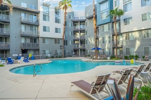 Ein modernes Apartmenthaus mit Swimmingpool, Liegestühlen und Palmen.