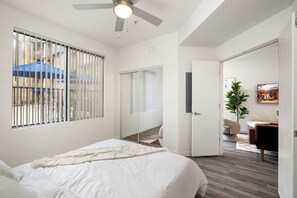 Ein modernes Schlafzimmer mit einem großen Bett, einem Deckenventilator und Blick durch ein Fenster mit Jalousien.