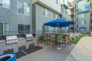 Eine Terrassenfläche mit Grill, Sitzgelegenheiten und Sonnenschirmen.