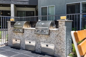 Eine moderne Grillstation im Freien mit mehreren Brennern und einem integrierten Lüftungssystem, vor einem Gebäude mit einem Balkon gelegen.