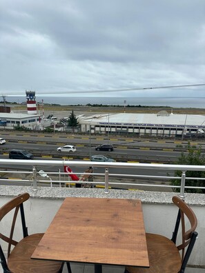 Vista desde un balcón con vistas a un aeropuerto, que incluye una torre de control, un edificio terminal y una carretera con vehículos.